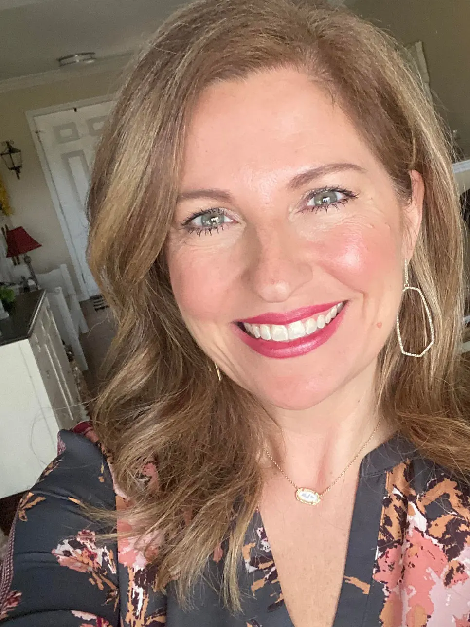 Smiling woman with shoulder-length light brown hair at Lenius Orthodontics in Overland Park, KS, wearing floral top and gold jewelry.