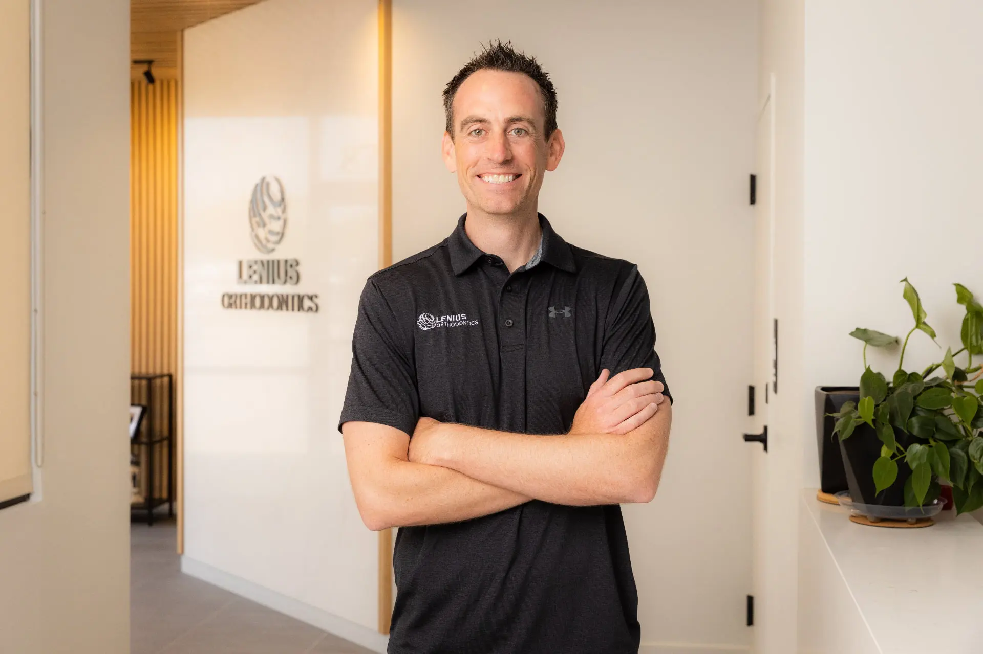 Dr. Jeffrey Lenius in a black polo shirt stands smiling with arms crossed, he is orthodontic expert at Lenius Orthodontics in Overland Park, KS.