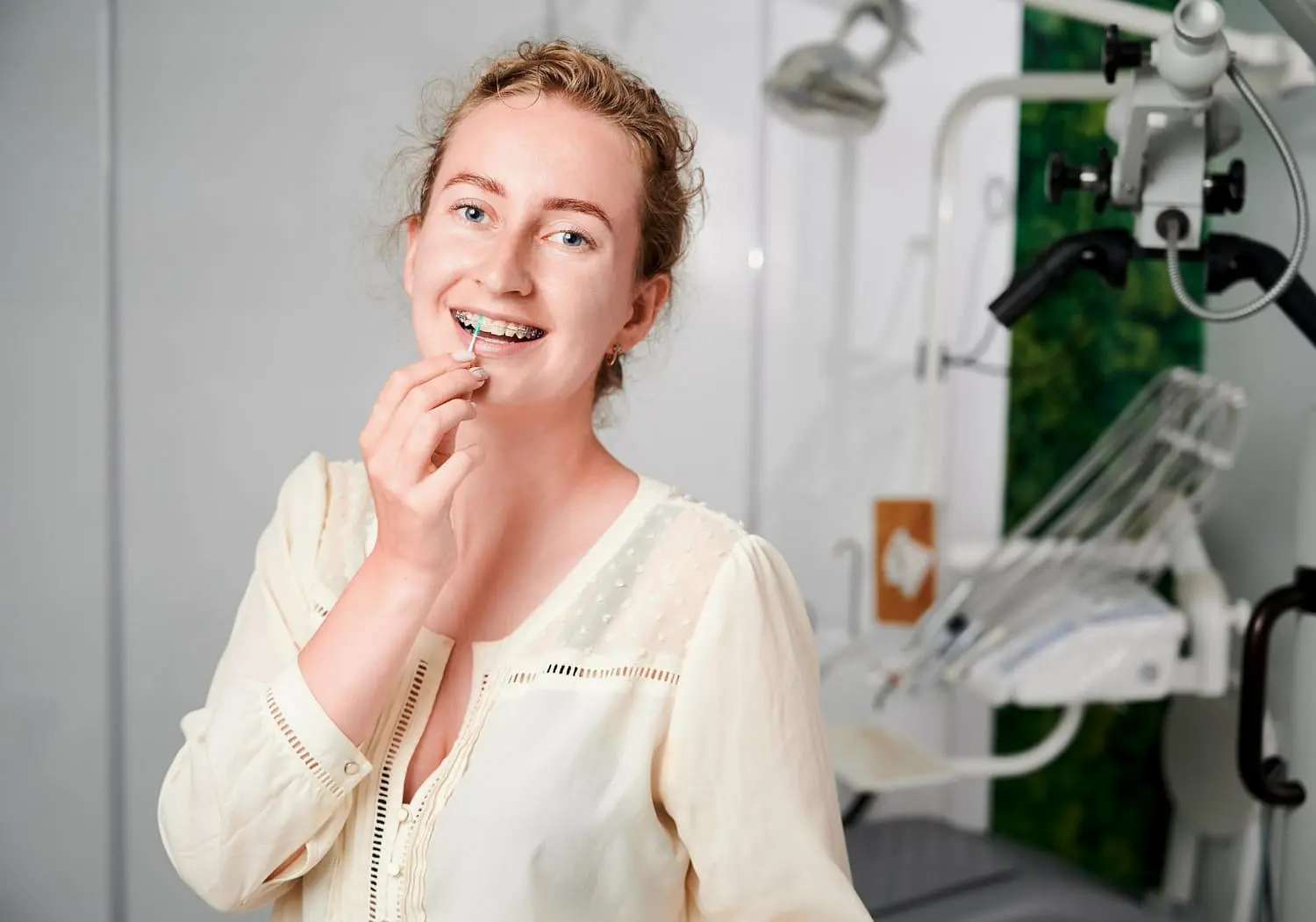 A young woman with ceramic braces at Lenius Orthodontics in Overland Park, KS, with dental equipment in the background.