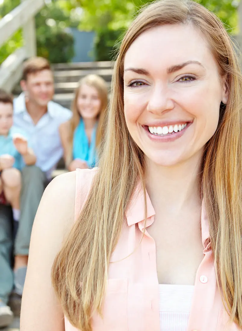 A woman smiles in front, representing braces cost at Lenius Orthodontics in Overland Park, KS, with three people blurred behind.