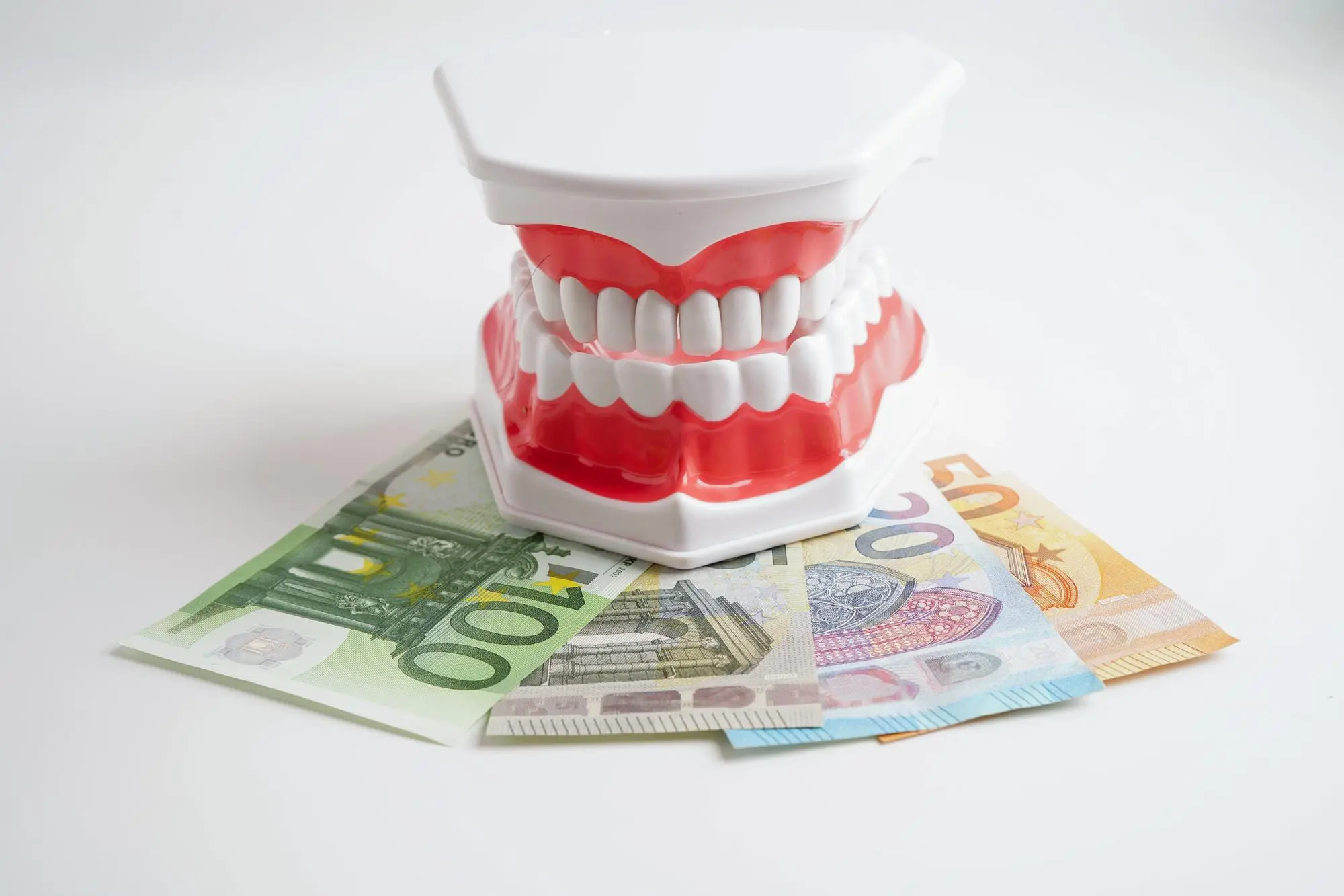 Euro banknotes with a teeth model on top highlight Lenius Orthodontics insurance costs in Overland Park, KS, against white.