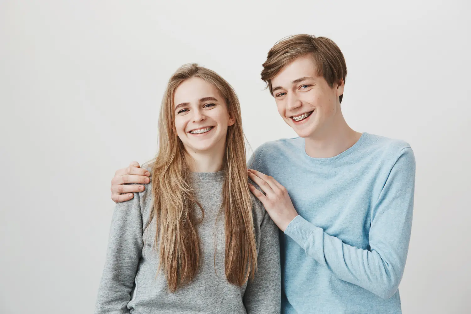 Smiling teens in light sweaters, one with a hand on the other's shoulder, represent affordable braces at Lenius Orthodontics in Overland Park, KS.