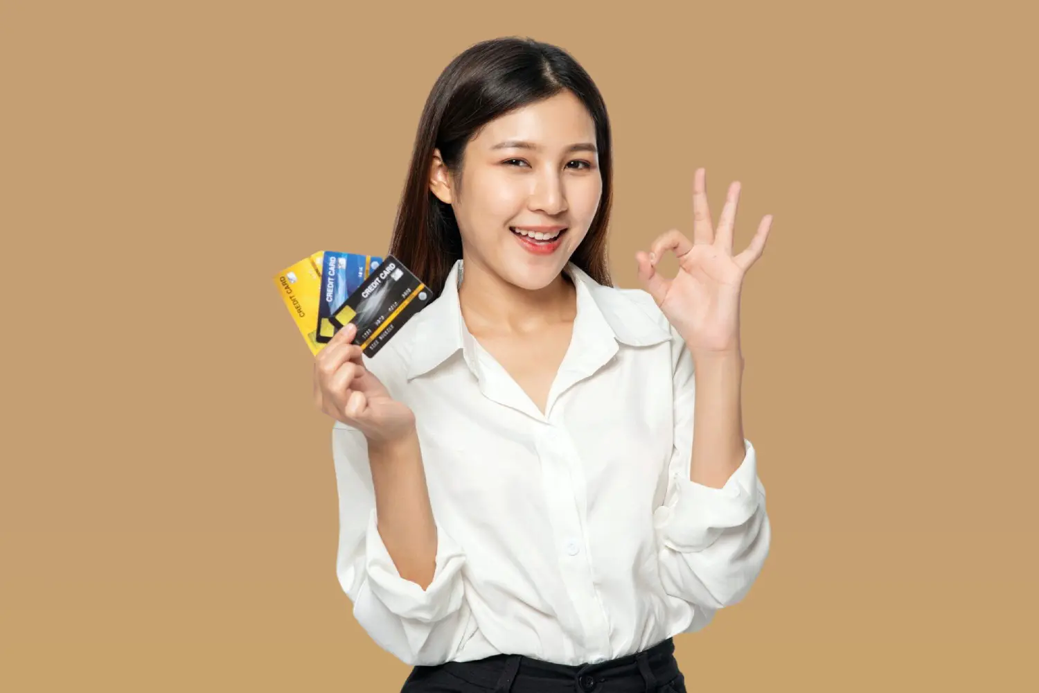 A smiling woman holds three credit cards and makes an "OK" gesture, promoting Lenius Orthodontics' Braces Payment Plan in Overland Park, KS.