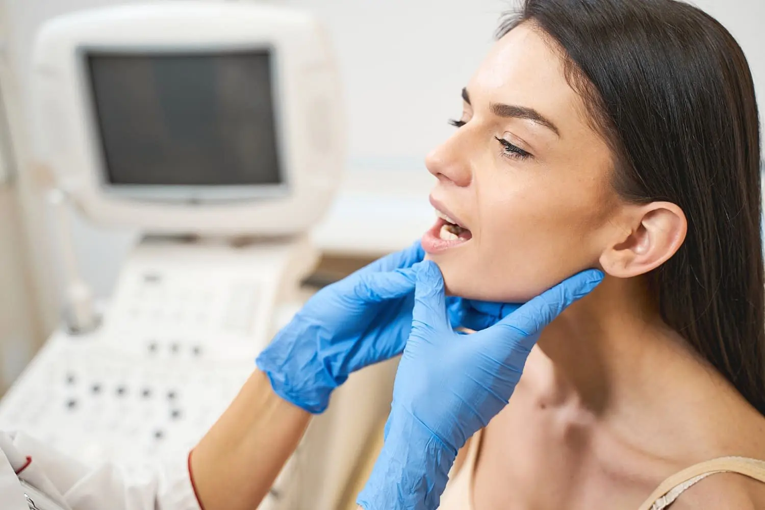 At Lenius Orthodontics in Overland Park, KS, a gloved professional examines a woman's jaw in an office with an ultrasound machine for plan jaw surgery.
