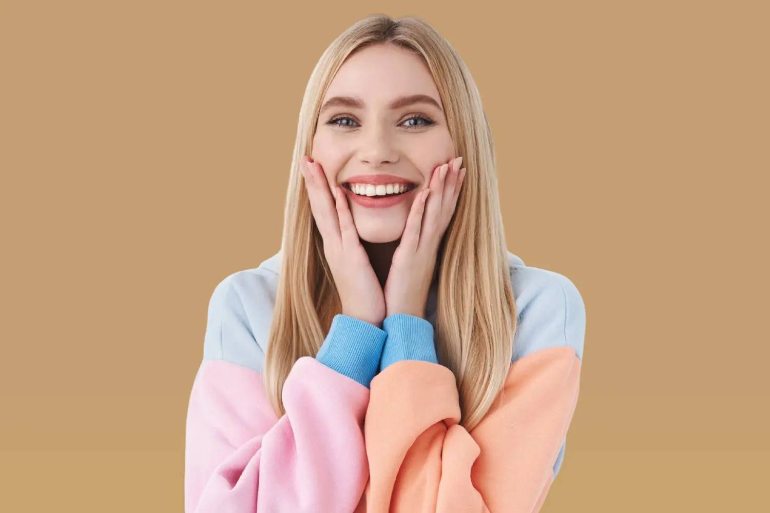 Smiling young woman with clear braces, pastel sweatshirt, and long blonde hair at Lenius Orthodontics in Overland Park, KS.