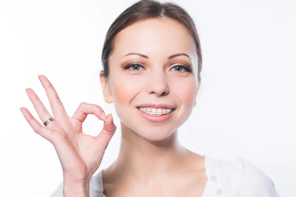 Smiling with clear braces, a young woman makes an "OK" gesture at Lenius Orthodontics in Overland Park, KS.