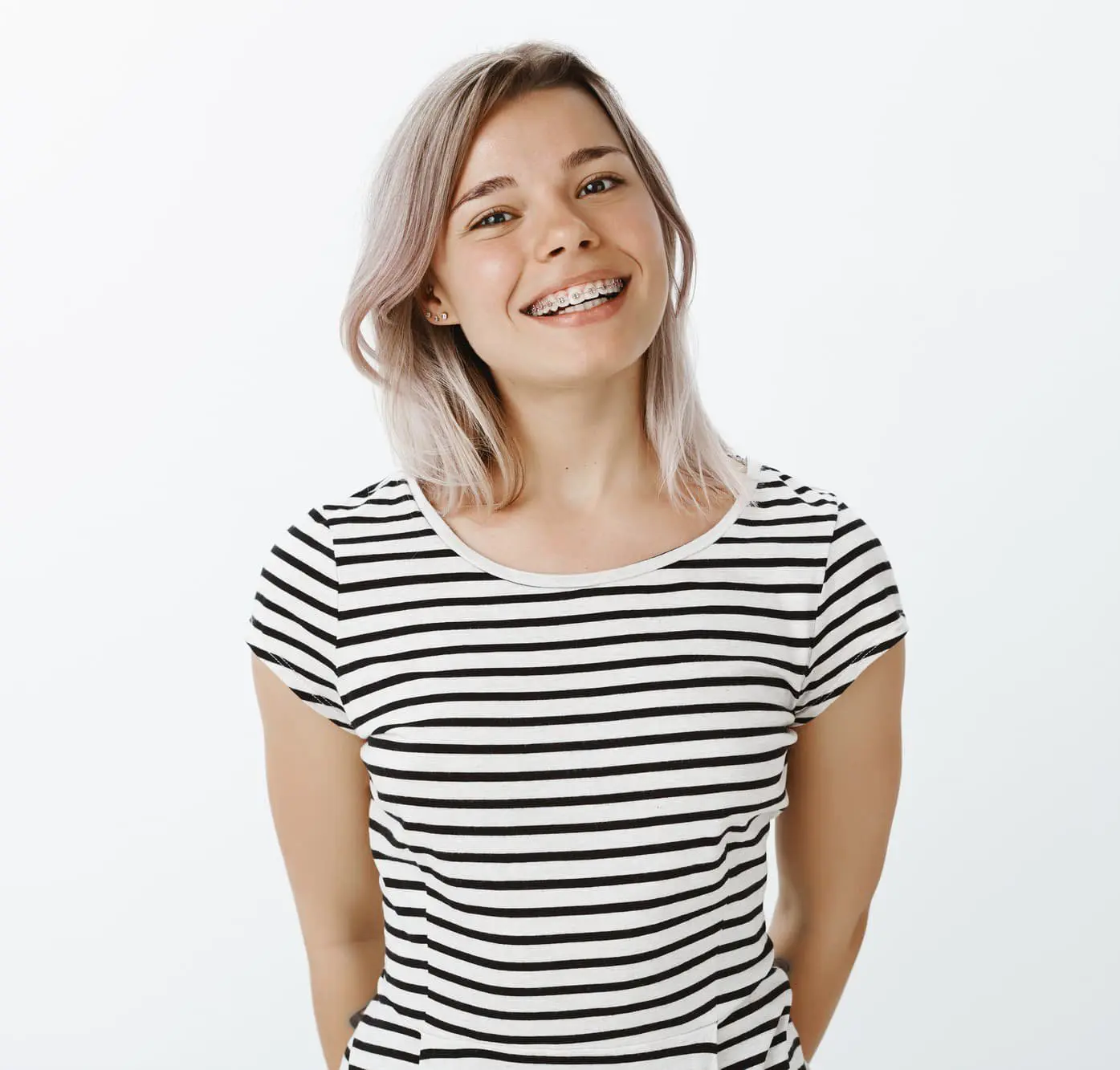 Smiling young woman with light hair and braces in a striped t-shirt promoting underbite treatment at Lenius Orthodontics in Overland Park, KS, against white.