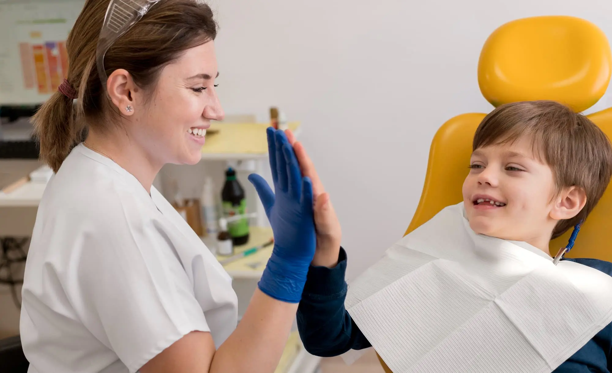 A pediatric orthodontist at Lenius Orthodontics in Overland Park, KS gives a high-five to a young boy in the dental chair, representing the ideal connection between patient, parent, and the right orthodontic care.