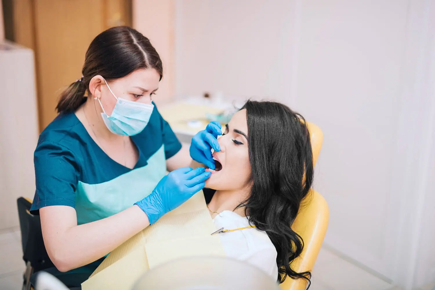 A dentist at Lenius Orthodontics in Overland Park, KS, wearing gloves and a mask, examines a female patient’s mouth exhibiting tongue thrust.