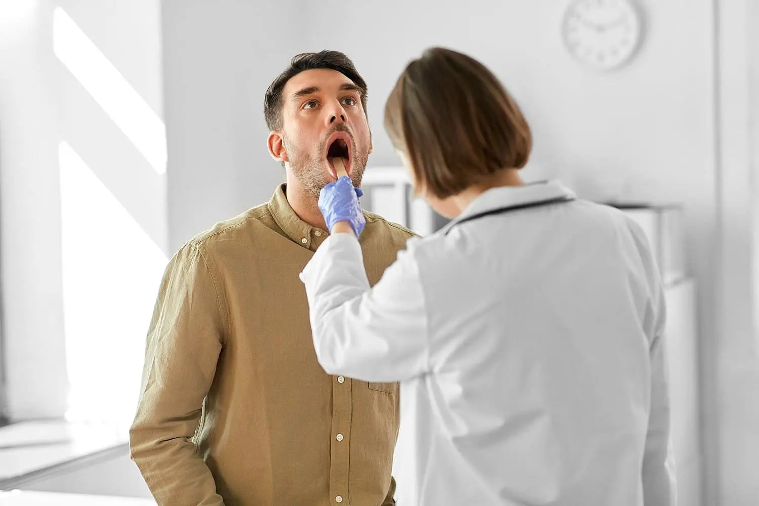 A healthcare professional at Lenius Orthodontics in Overland Park, KS examines a man's open mouth exhibiting tongue thrust with a tongue depressor.