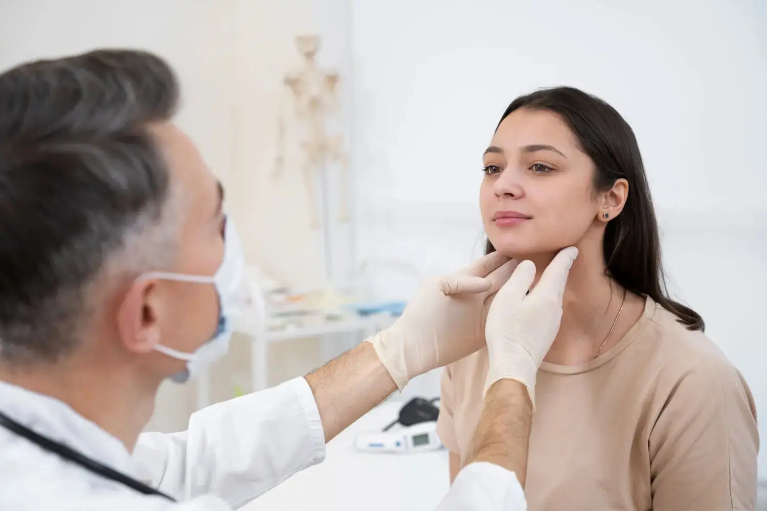 In Overland Park, KS at Lenius Orthodontics, a doctor in gloves examines a woman's neck as she looks ahead during a checkup for Jaw Surgery.