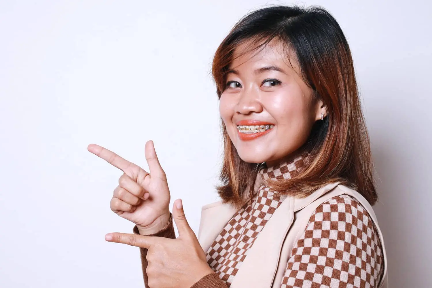 Smiling woman with braces points left against a white background, highlighting the Braces Payment Plan and flexible plans from Lenius Orthodontics in Overland Park, KS.