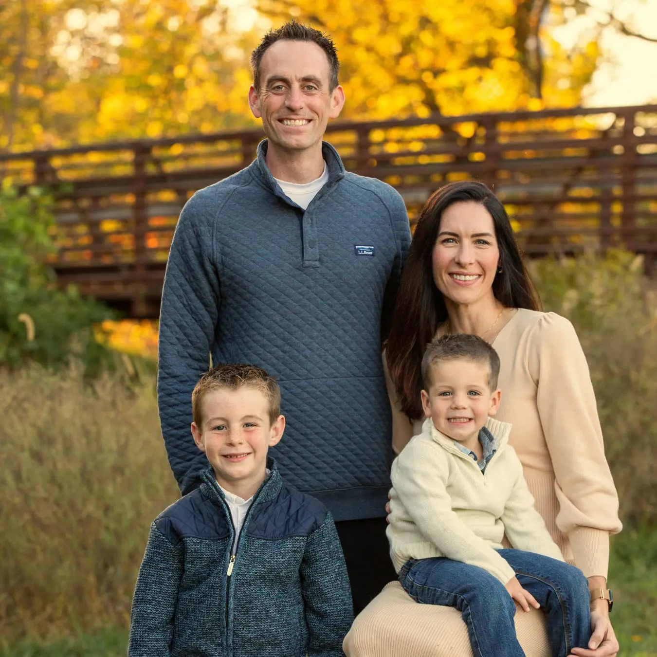 A family of Dr. Jeffrey Lenius poses by a wooden bridge and falling leaves in Overland Park, KS. Dr. Jeffrey Lenius is an orthodontic expert at Lenius Orthodontics.