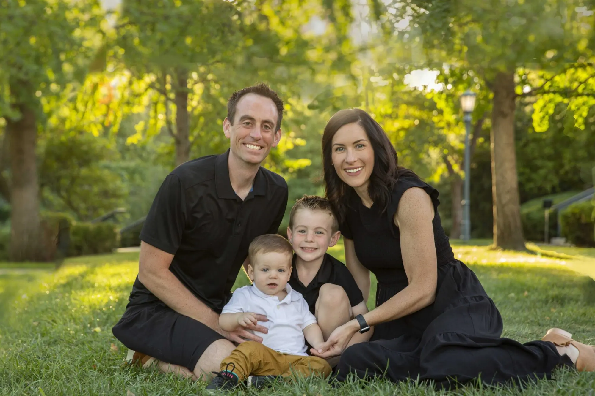 Smiling Dr. Jeffrey Lenius family of four on grass in Overland Park, KS; parents in black, kids between them, trees behind.