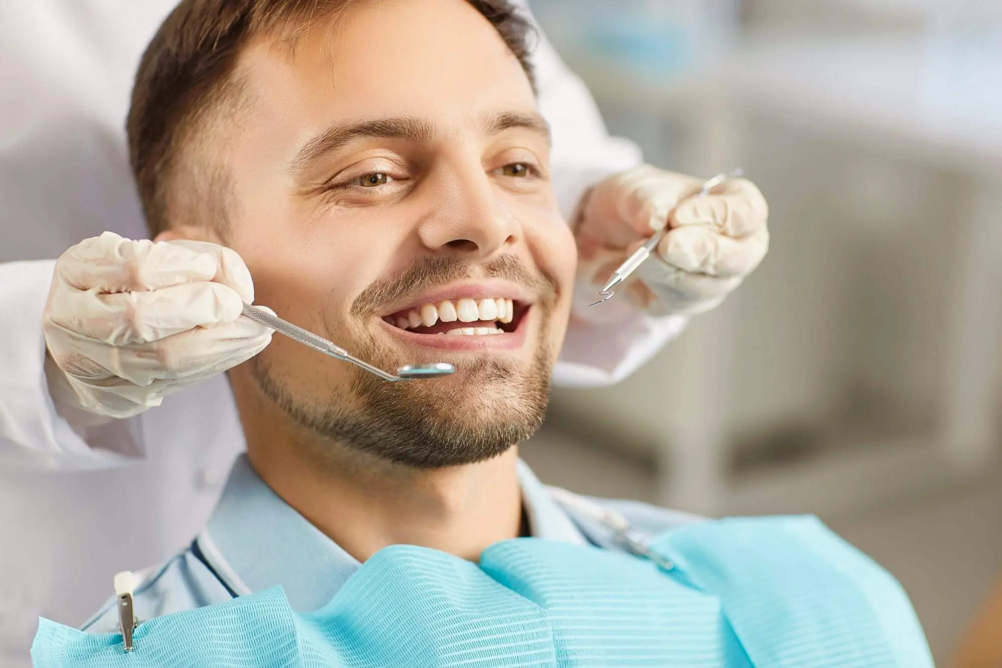 At Lenius Orthodontics in Overland Park, KS, a man smiles represent orthodontic treatment for mouth breather in a dental chair as the dentist examines his teeth with instruments.
