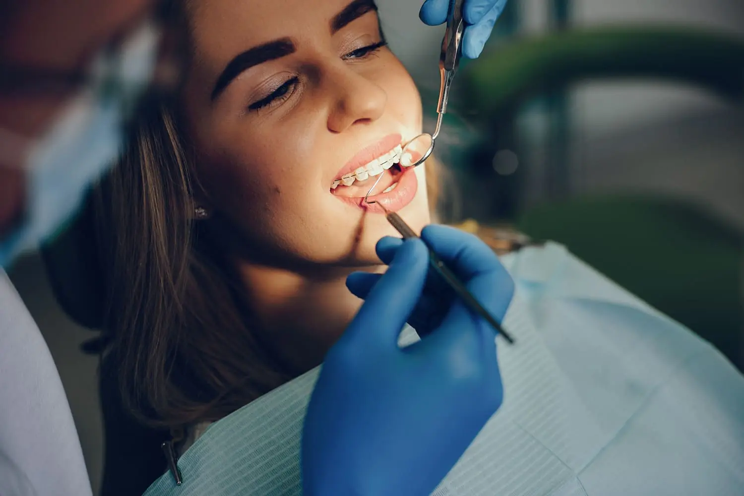 A dentist at Lenius Orthodontics in Overland Park, KS checks a woman's teeth, discussing Clear Braces options with her.
