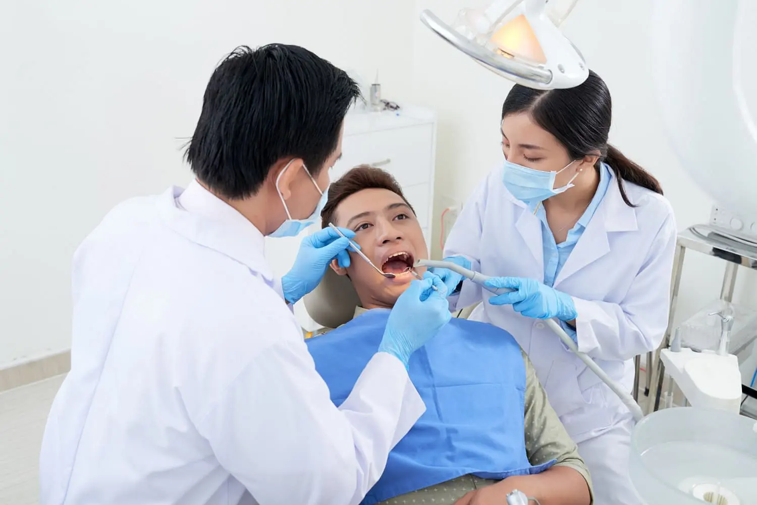 At Lenius Orthodontics in Overland Park, KS, two masked dentists perform a dental procedure tongue thrust treatment on a patient under exam lights.