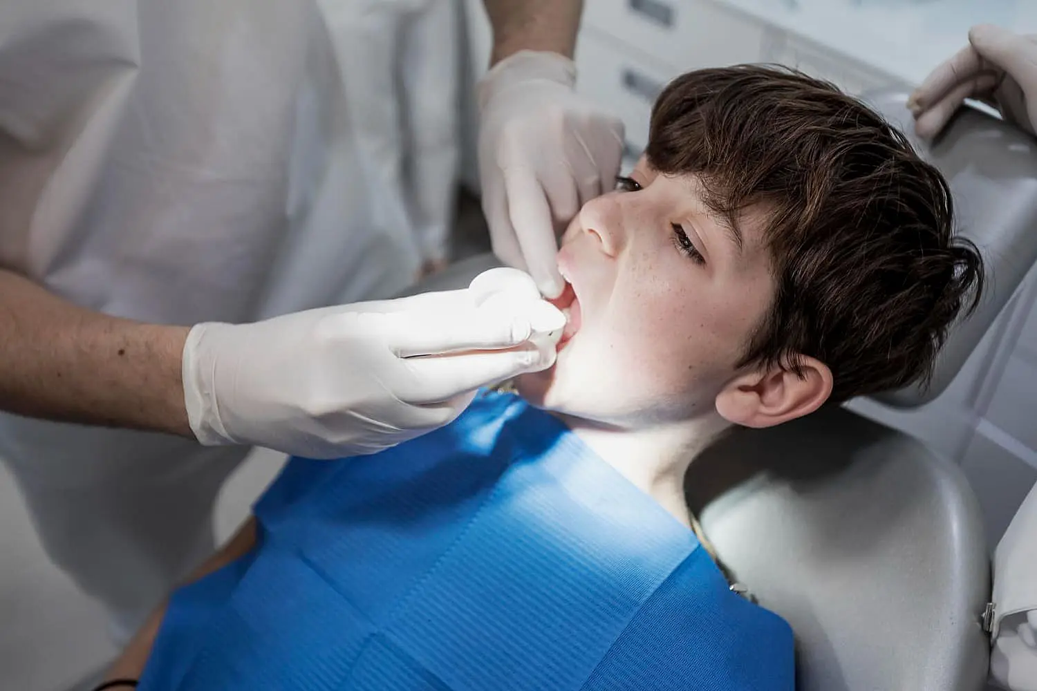 A young boy in a dentist's chair with a blue bib gets his mouth examined for tongue thrust treatment at Lenius Orthodontics in Overland Park, KS.
