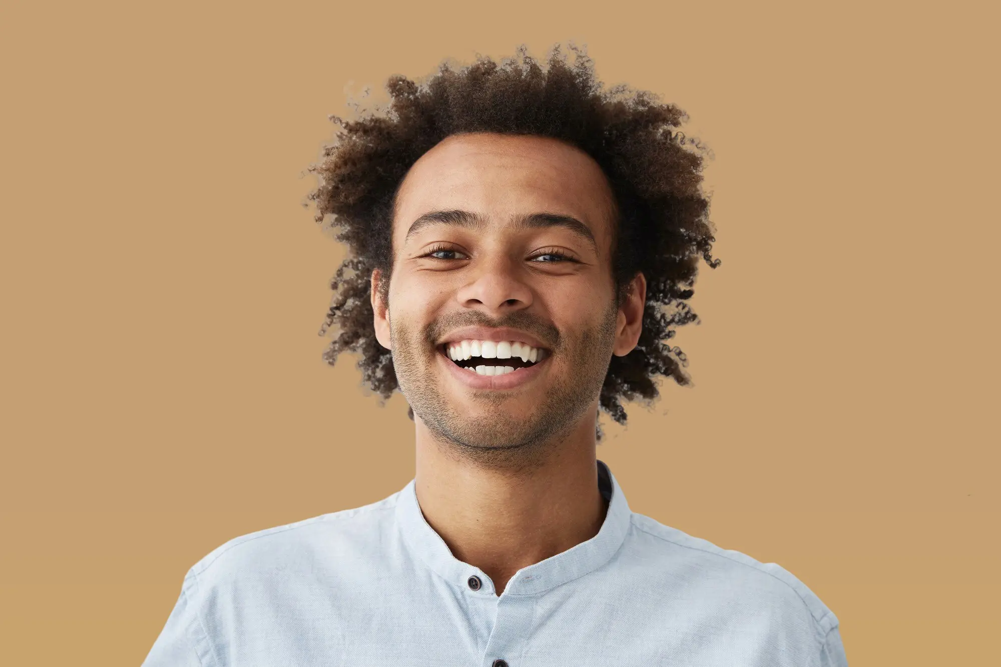 A young man with curly hair smiles at the camera in a light shirt, shown orthodontic treatment for mouth breather for Lenius Orthodontics in Overland Park, KS.