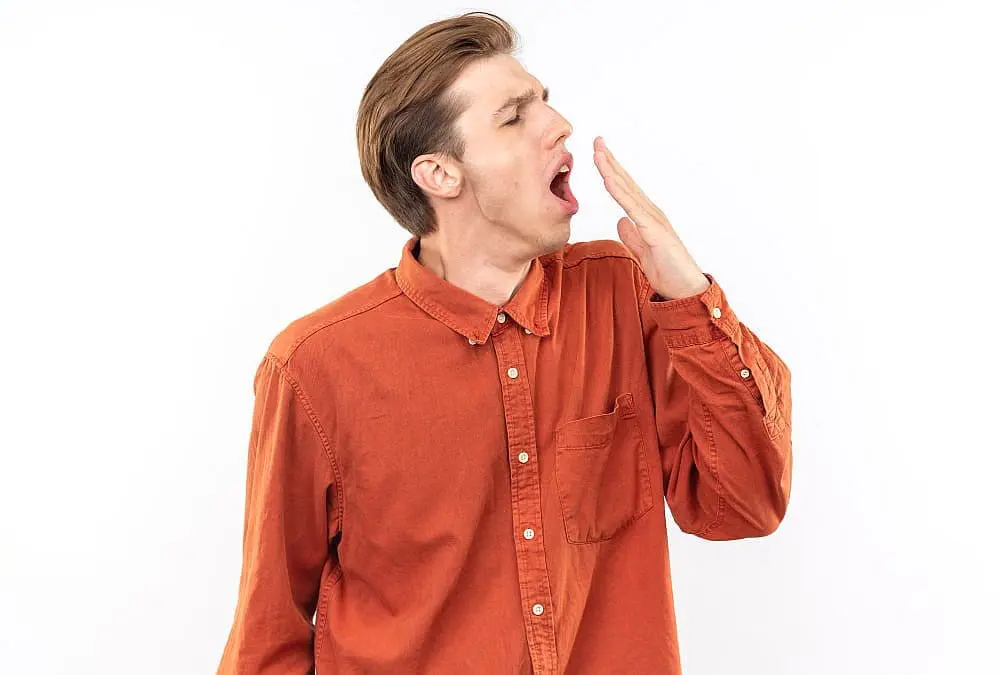 A person in an orange shirt yawns, represent mouth breathing and its relationship to underbite at Lenius Orthodontics in Overland Park, KS, against a white background.