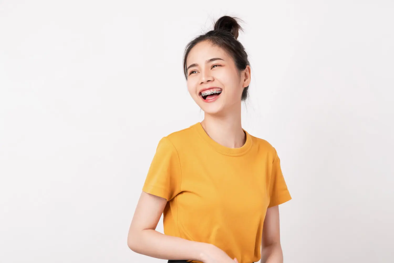 A young woman with braces in a yellow t-shirt smiles confidently, supported by Orthodontic Insurance Plans at Lenius Orthodontics in Overland Park, KS.