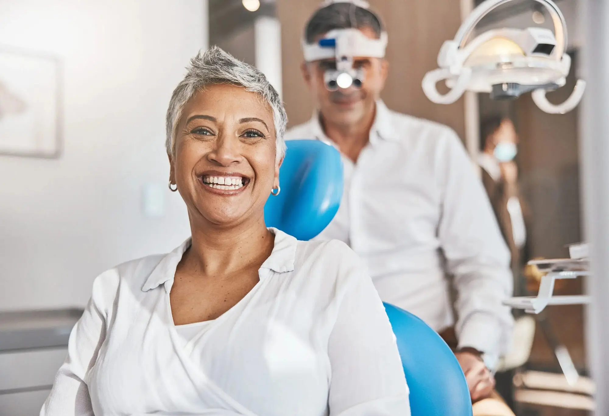 At Lenius Orthodontics in Overland Park, KS, a smiling woman sits in a dental chair with a Adult Orthodontics behind her wearing loupes.
