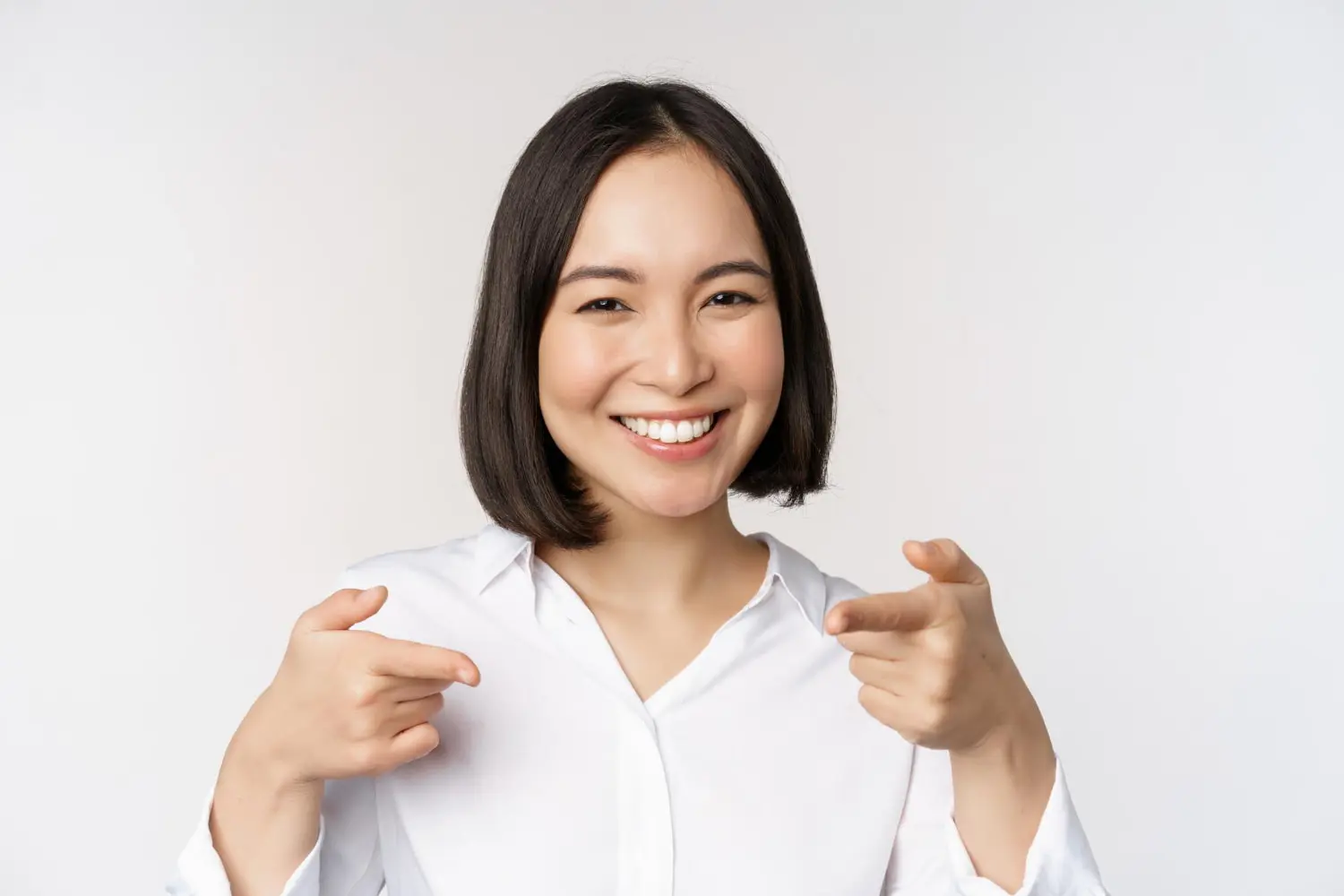 Smiling woman with metal braces points at the camera for Lenius Orthodontics in Overland Park, KS, on a plain white background.