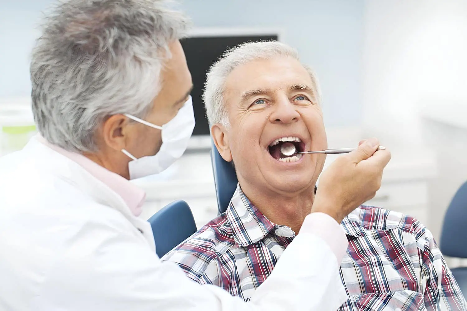 In a bright clinic, a dentist checks an older man's teeth with a mirror represent consultation about jaw surgery at Lenius Orthodontics in Overland Park, KS.