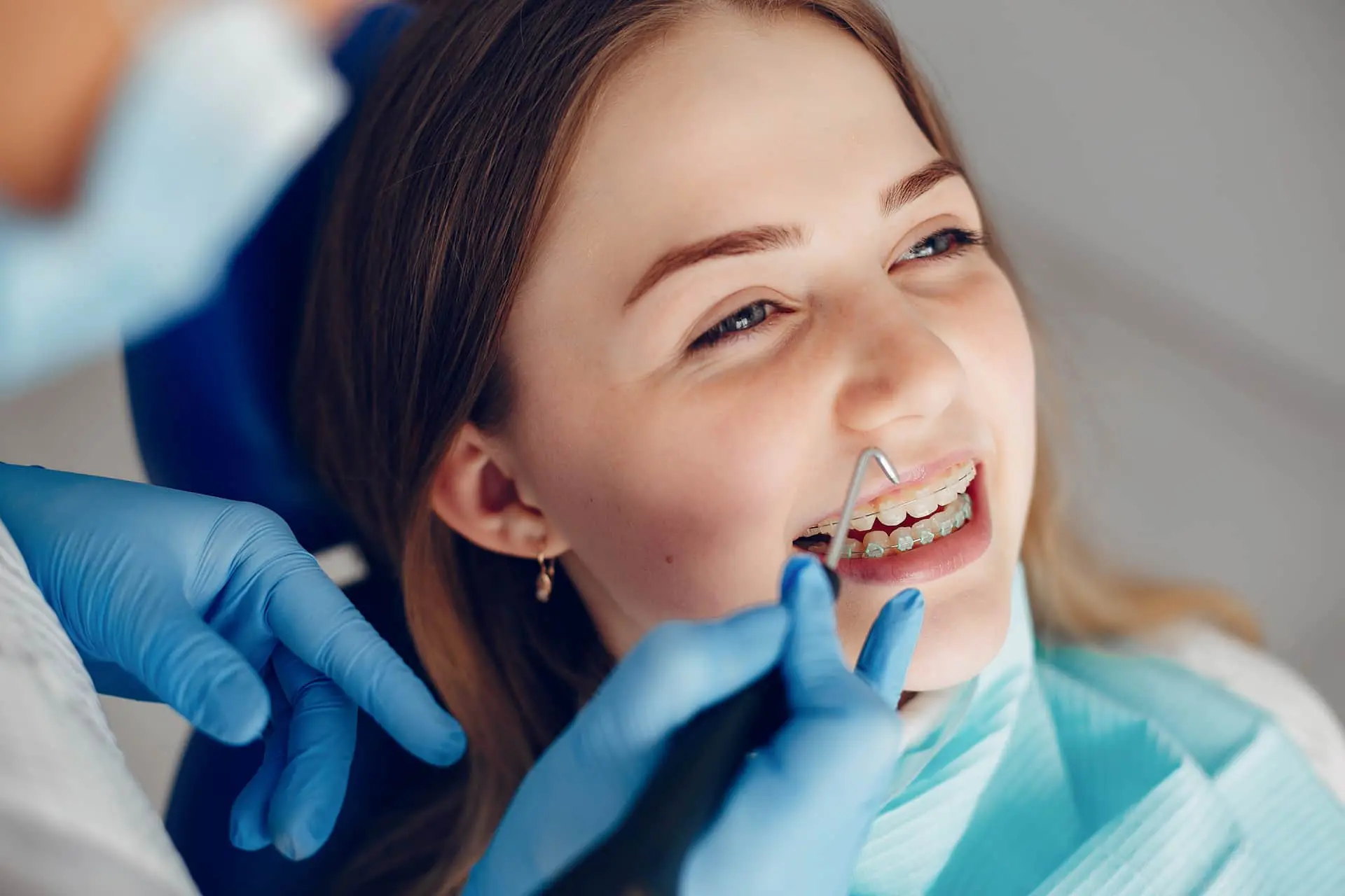 A dentist at Lenius Orthodontics in Overland Park, KS checks a smiling patient's clear braces with blue gloves and dental tools.