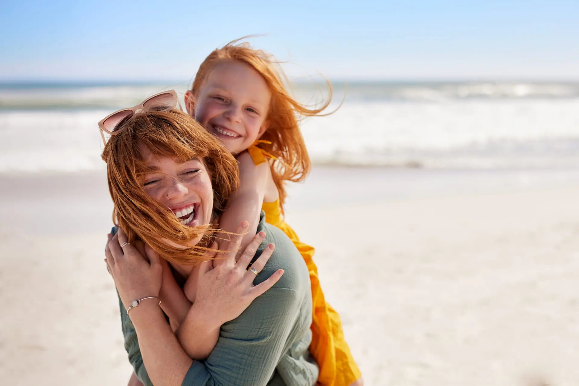 At the beach in Overland Park, KS, a woman representing the best metal braces carries a smiling girl on her back by the shoreline.