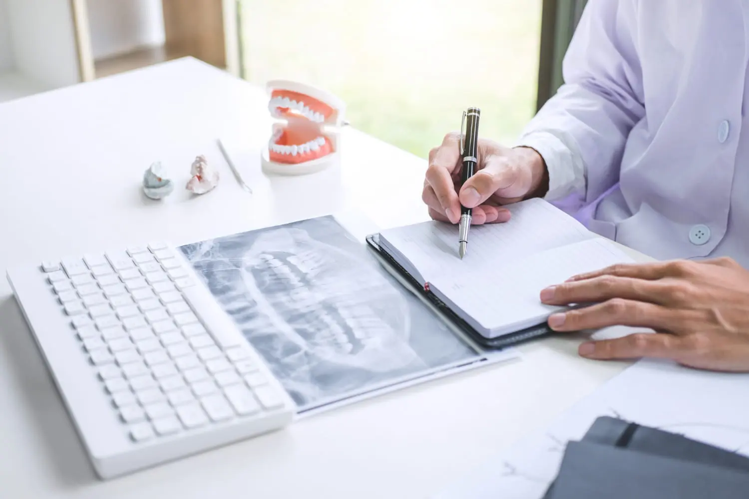 At a desk in Overland Park, KS, Lenius Orthodontics staff writes in a notebook, showcasing Orthodontic Insurance Plans with dental x-rays, models, and insurance info nearby.