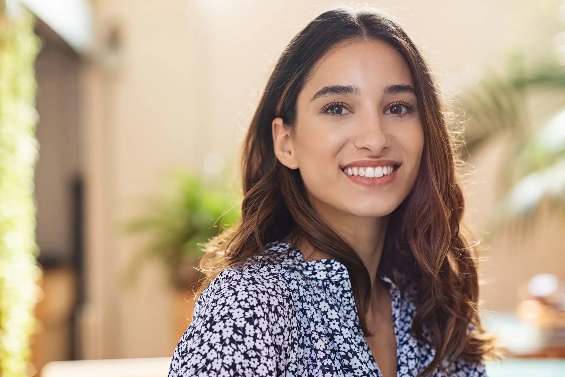 Smiling woman with result adult braces at Lenius Orthodontics in Overland Park, KS; blue floral blouse, green plants blurred behind her.