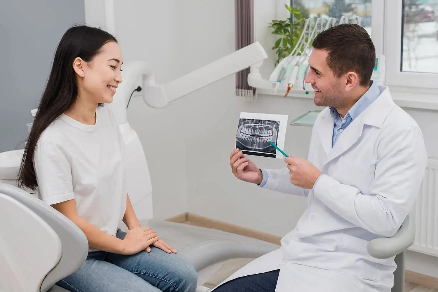 A dentist at Lenius Orthodontics in Overland Park, KS discusses a dental X-ray for Jaw Surgery with a seated female patient in the clinic.