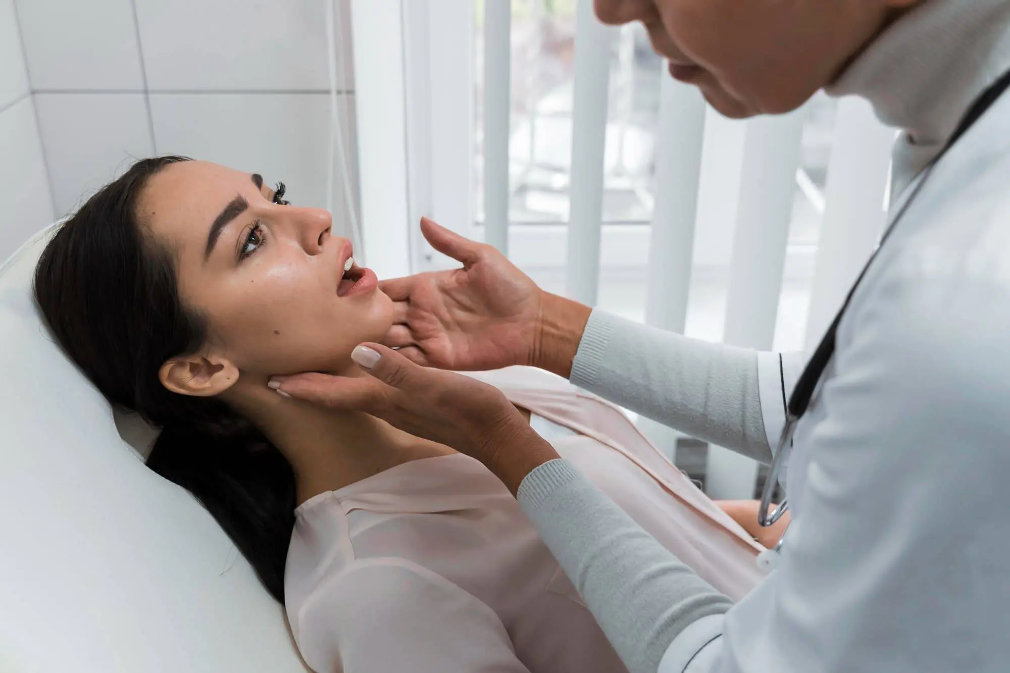 A doctor at Lenius Orthodontics in Overland Park, KS examines a woman's jaw and neck as she sits in a medical chair, looking up for rehabilitation exercises after jaw surgery.
