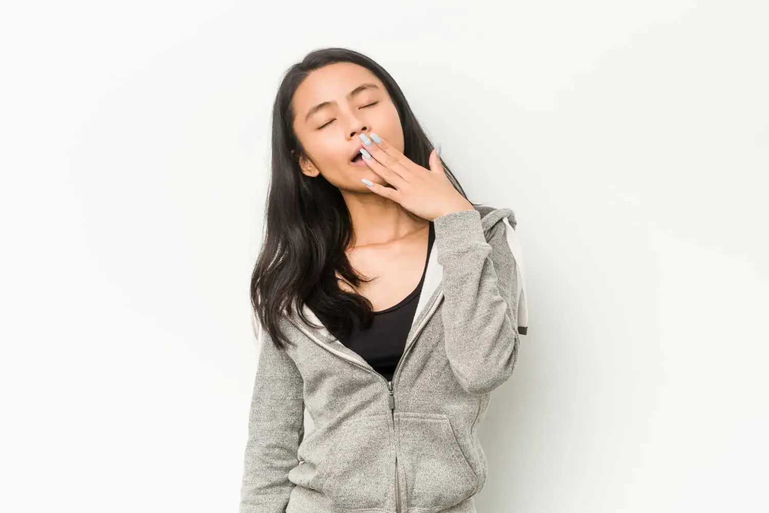 A person with long dark hair in a grey hoodie yawning show mouth breather at Lenius Orthodontics in Overland Park, KS, against a white background.