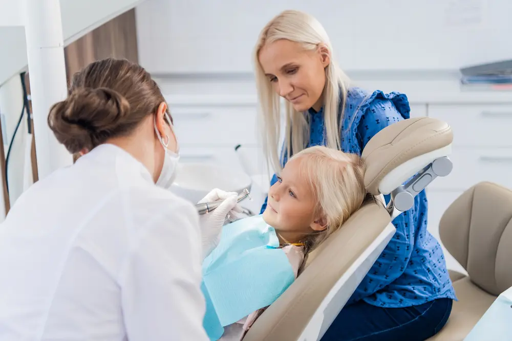 a blonde mother accompanying her child while she's been examined by the orthodontist after being explained about how to fix overbite in overland park, KS
