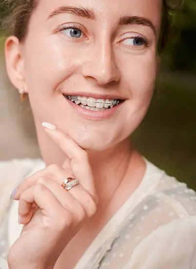 Smiling person with braces correcting an overbite at Lenius Orthodontics in Overland Park, KS, chin on hand, light features.