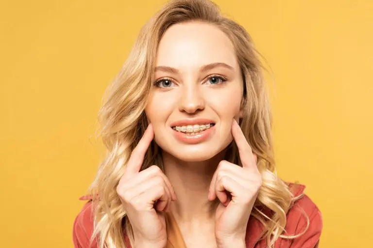 Smiling young woman with long blonde hair points at her clear braces, promoting Lenius Orthodontics in Overland Park, KS, on yellow.