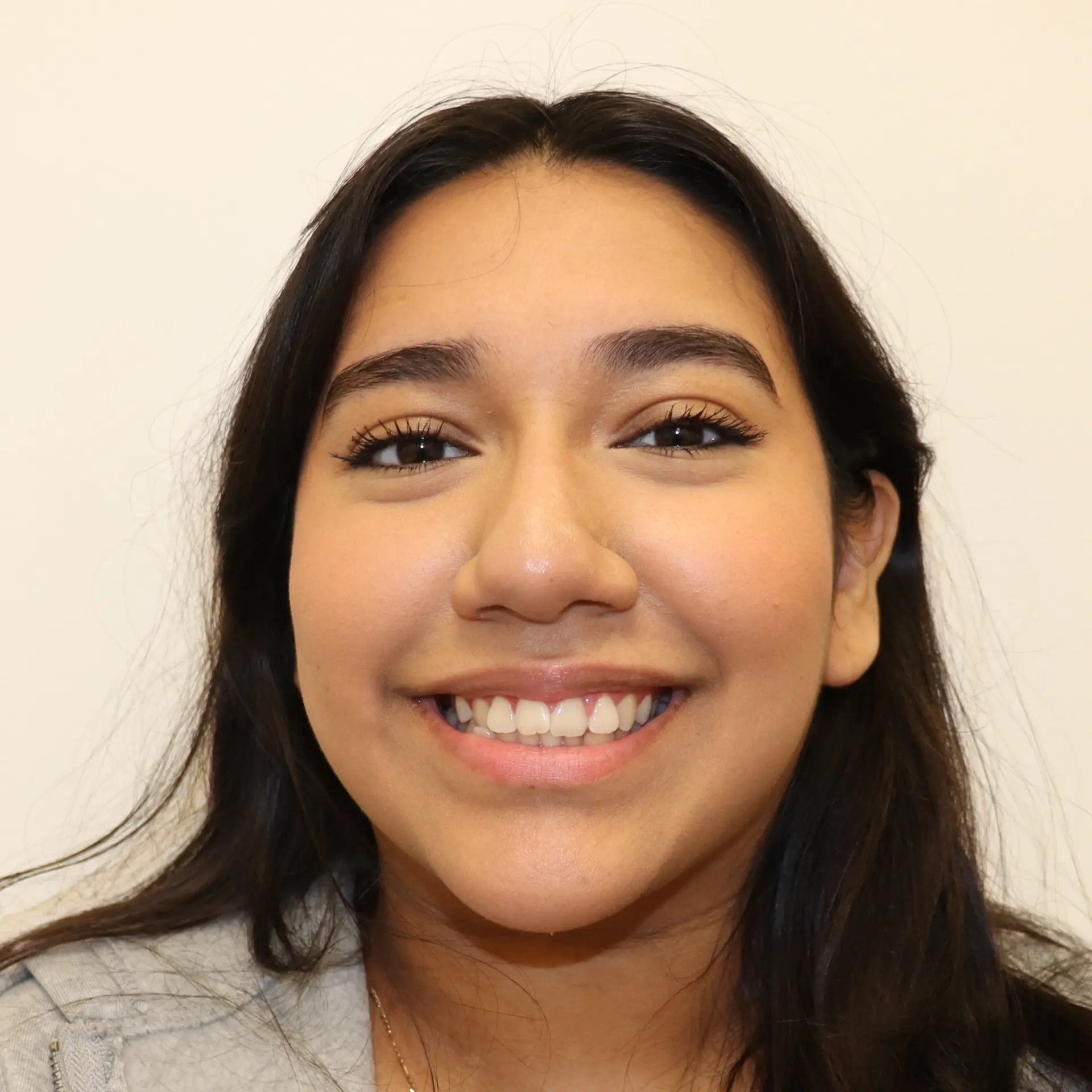 A young woman with long dark hair smiles at the camera, representing before dental care with braces at Lenius Orthodontics in Overland Park, KS.