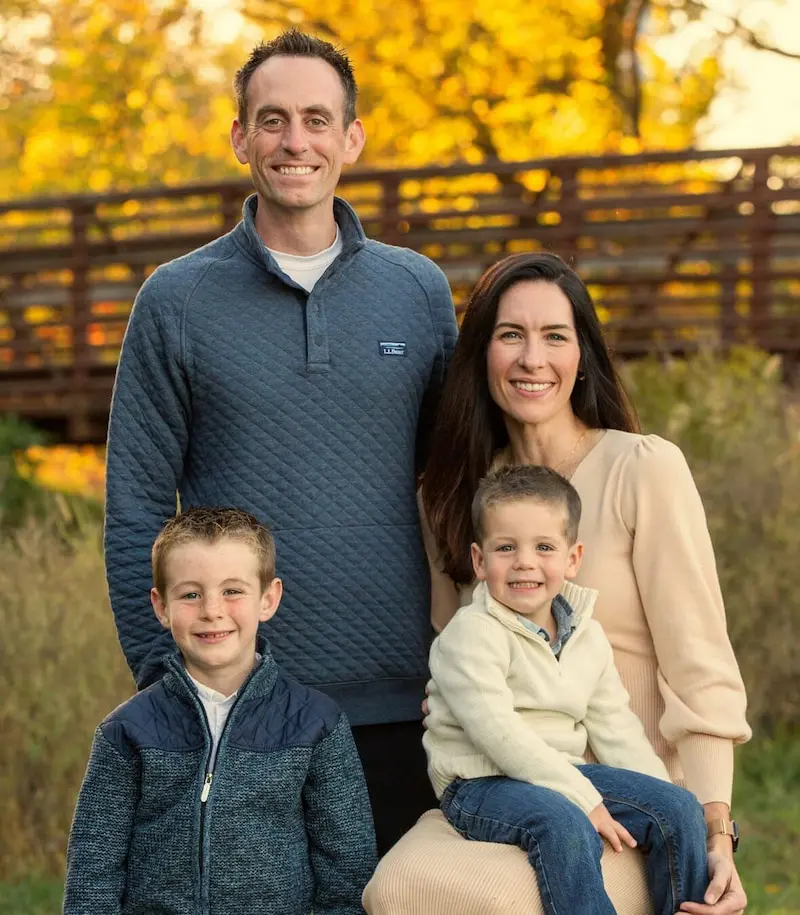 A family of Dr. Jeffrey Lenius poses by a wooden bridge and falling leaves in Overland Park, KS. Dr. Jeffrey Lenius is an orthodontic expert at Lenius Orthodontics.