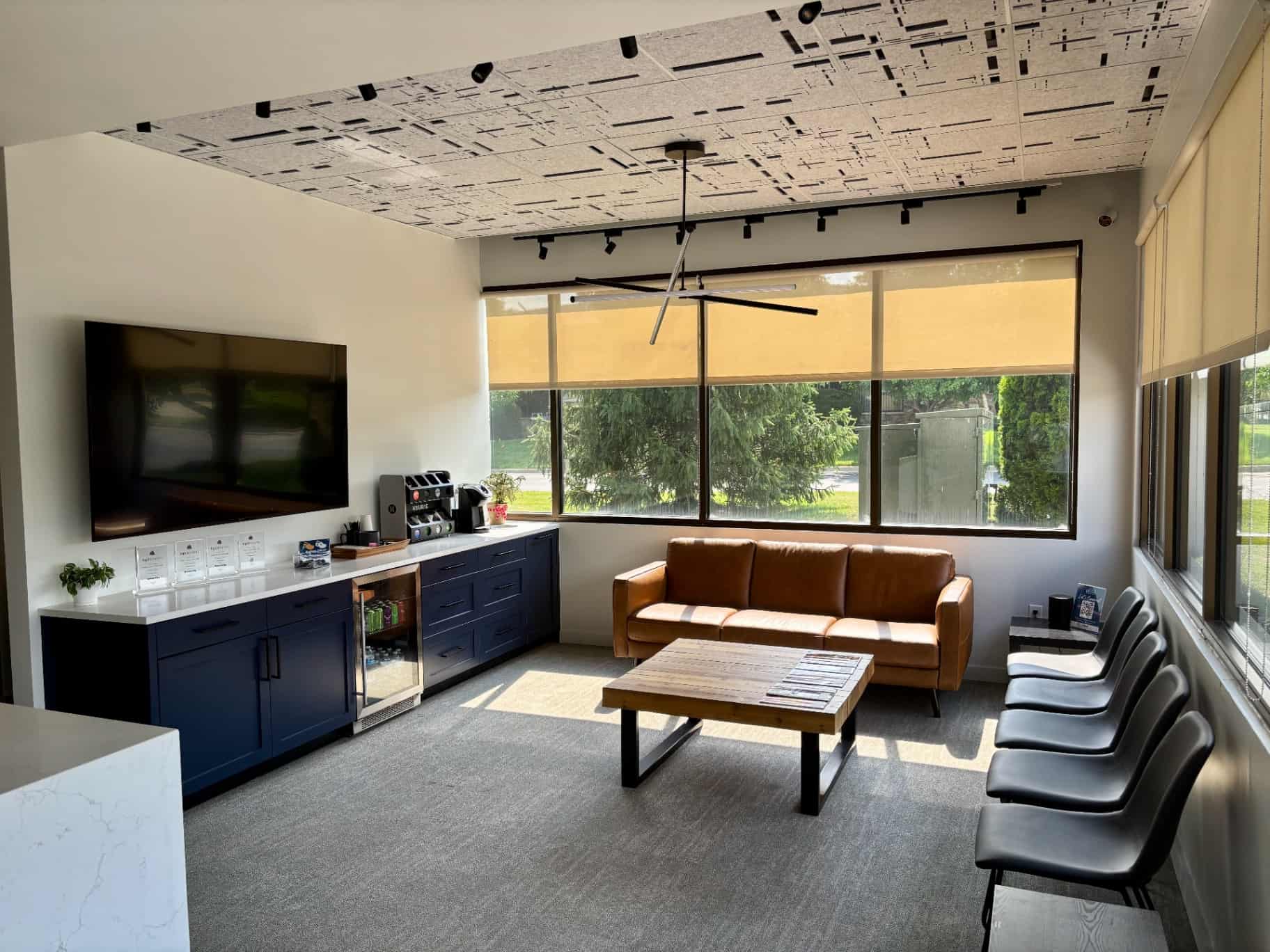 A stylish lounge at Lenius Orthodontics in Overland Park, KS features Orthodontic Insurance Plans, leather sofa, black chairs, TV, coffee station, and large windows.