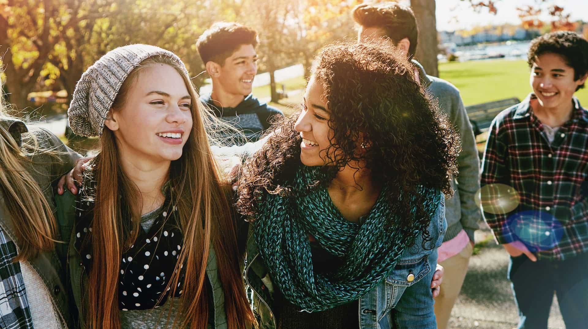 Teens walk outside on a sunny day, chatting about school and Adult Orthodontic Treatment from Lenius Orthodontics in Overland Park, KS, with trees and grass behind.