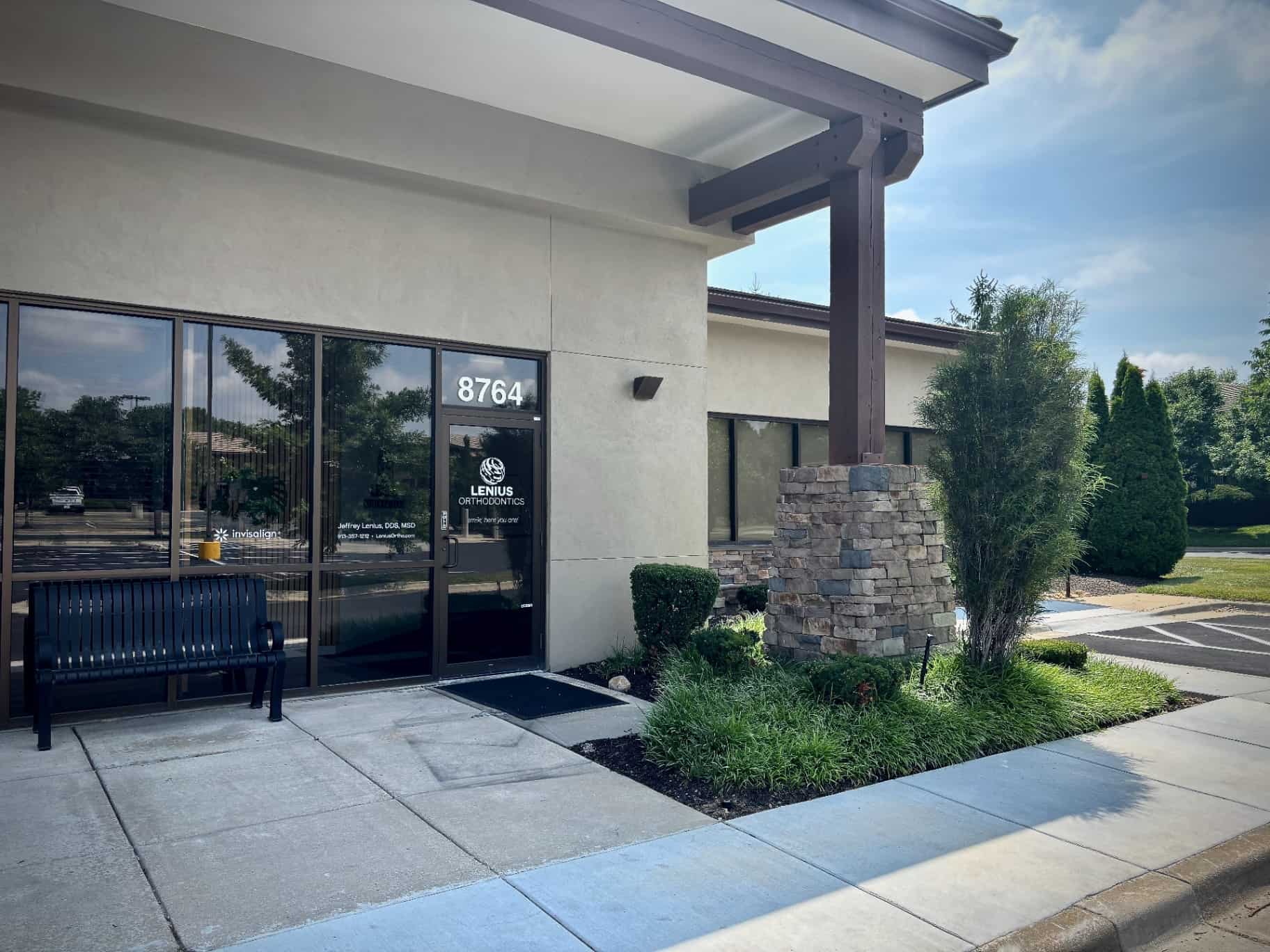 Lenius Orthodontics in Overland Park, KS at 8764 features a glass entrance, black bench, greenery, and stone pillar entryway.